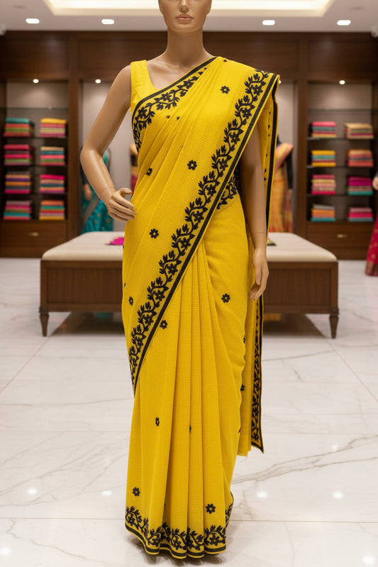 A bright yellow saree or fabric drape with black floral border embroidery and small black flower motifs.