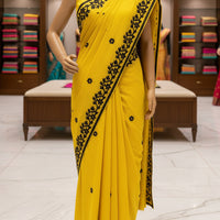 A bright yellow saree or fabric drape with black floral border embroidery and small black flower motifs.